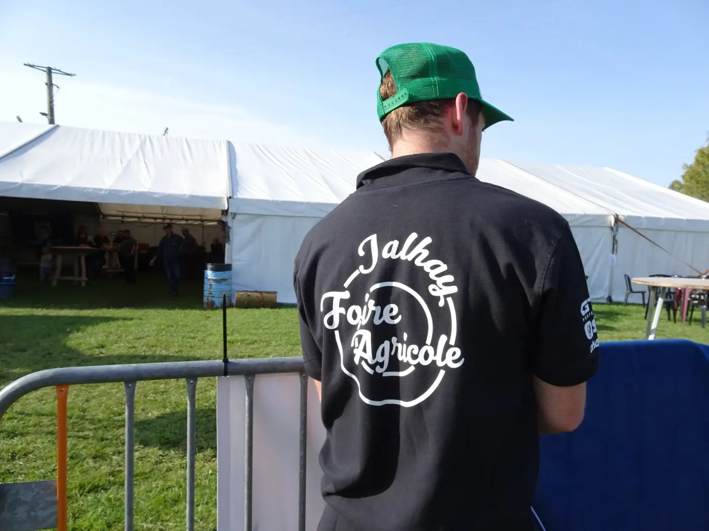 Bénévole en t-shirt « Foire agricole Jalhay » face aux chapiteaux de la foire